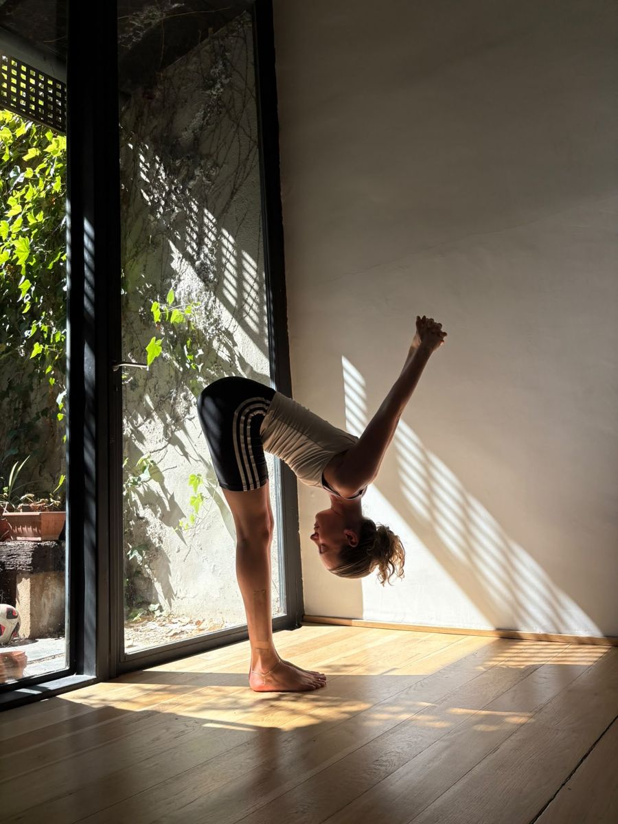 Cos in a standing forward bend by a sunlit window